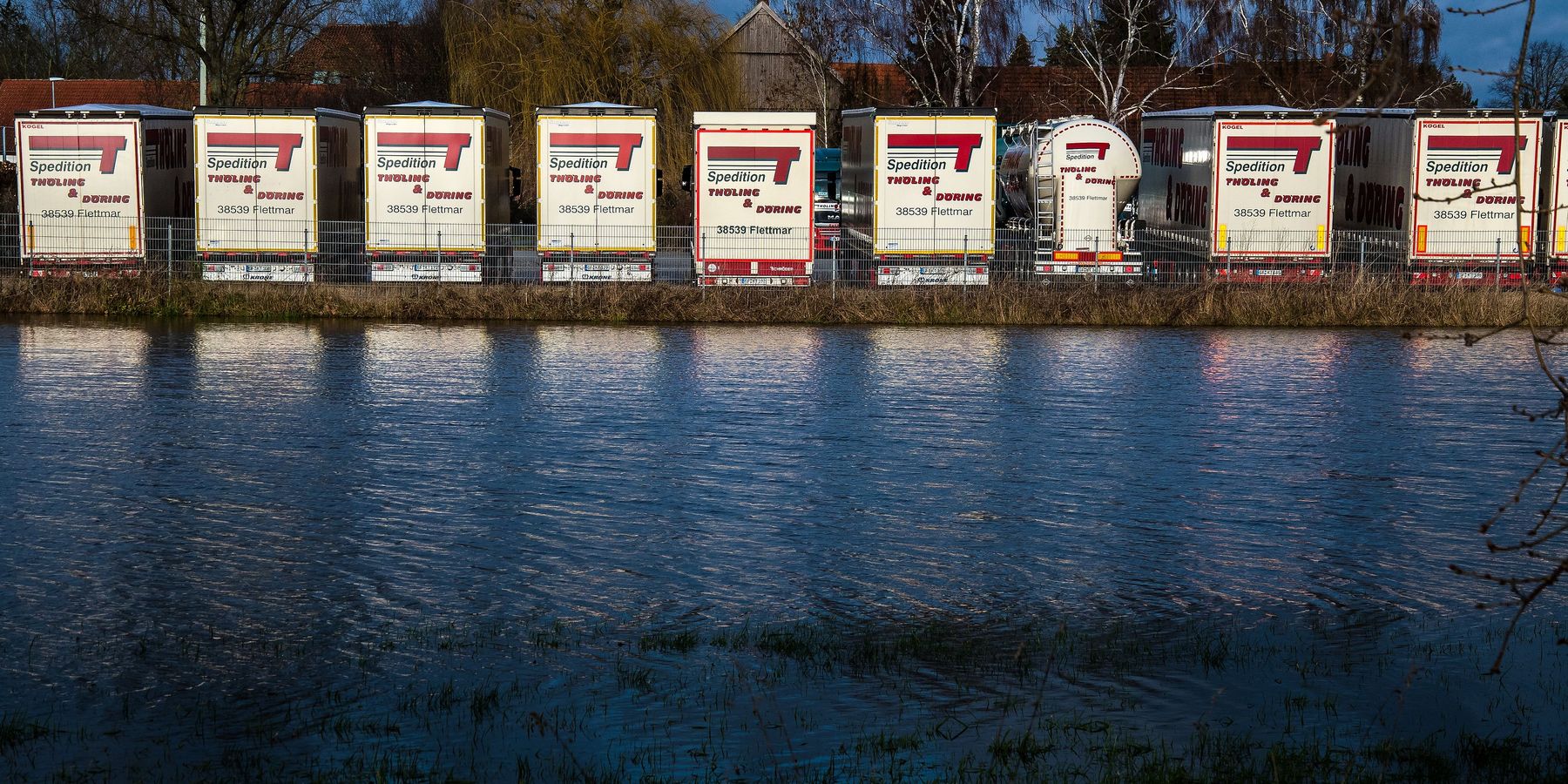 Aufliegerreihe der Spedition am Ufer der Aller